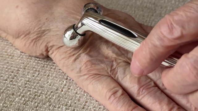 Elderly hands massager rollers closeup showcasing grandmother gently rolling silver dual roller across wrinkled skin on textured