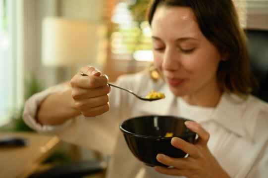 Close-up shot of a Young Caucasian woman eating breakfast cereal from a bowl, enjoying a simple and healthy morning routine at home