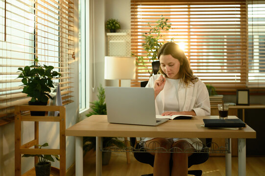 Caucasian woman concentrating on tasks in her home office, combining digital work and note-taking