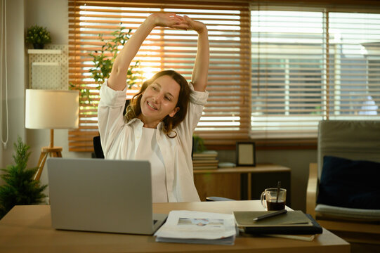 Young Caucasian woman stretching her arms while taking a break from work in a bright home office