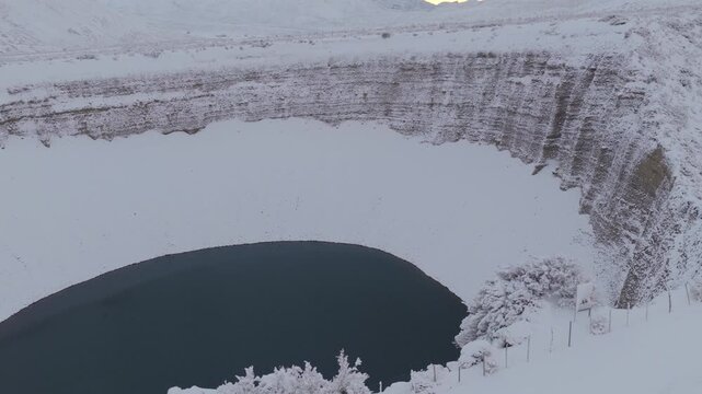 Close aerial view of Pozo de las Animas sinkhole in Mendoza Argentina showing deep crater walls frozen landscape and dark water contrast in winter.