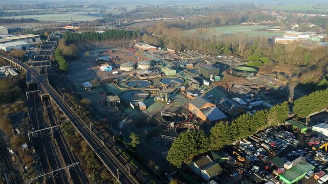 High-angle drone perspective of expansive manufacturing warehouses adjacent to a busy railway junction in Rugby England.