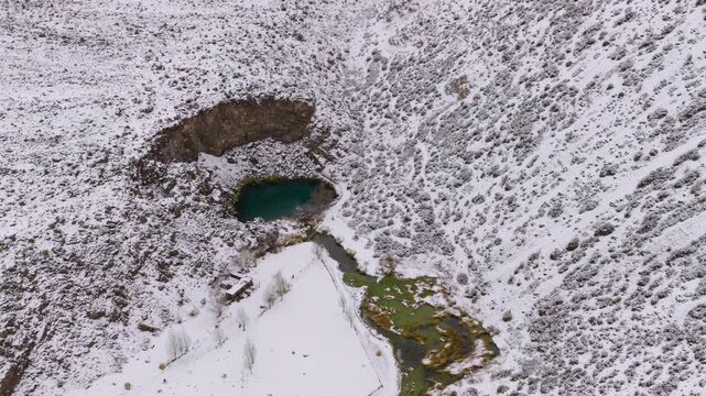 Top aerial view of Laguna de la Ni&ntilde;a Encantada in Malargue Mendoza showing crater shape turquoise water and snow covered geological landscape.
