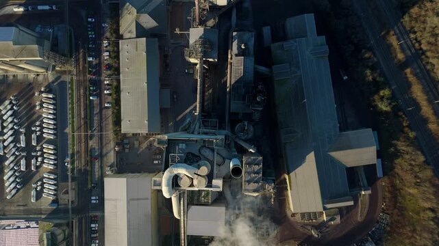 Smooth aerial drone glide over the complex industrial piping and kilns of a cement facility.