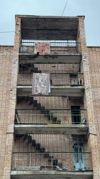 Brick building exterior hanging carpets balconies, weathered hostel end with open staircases and concrete landings, patterned rugs.