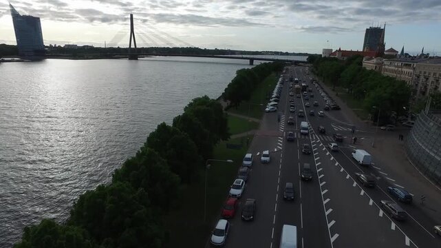 Wide aerial drone panoramic view of Riga city sunset over Daugava river featuring Van&scaron;u Bridge and Swedbank headquarters under dramatic cloudy sky with evening traffic flow on 11. novembra krastmala