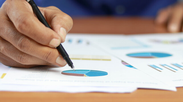 Close-up of hand analyzing business charts and financial reports with pen, representing data analysis, market research, strategic planning, investment management, corporate performance 