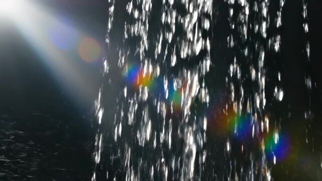 Water droplets falling with light and rainbow effect.