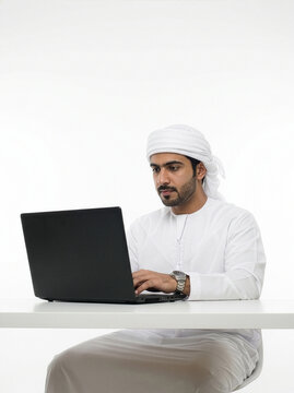 Low angle Emirati businessman with shemagh and agal using laptop in minimal white setting