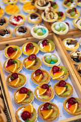 Fototapeta premium Assorted dessert cups with fruit and chocolate displayed in market stall, colorful sweet selection with orange kiwi grapes and mango, ready for sale in street food setting
