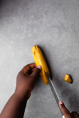 Overhead view of ripe plantains being peeled on grey countertop, top view of peeling overripe yellow plantains on grey background, ripe plantains being prepared for frying © this_baker