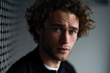 Obraz premium A contemplative young man with curly hair gazes thoughtfully into the distance, evoking a sense of introspection and depth against a muted background.