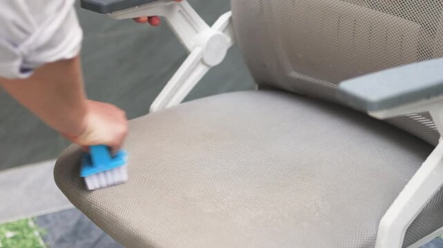 Scrubbing office chair with blue brush effectively removes stains from fabric. Person applies pressure to mesh seat for deep cleaning. This scrubbing office chair routine keeps furniture new.