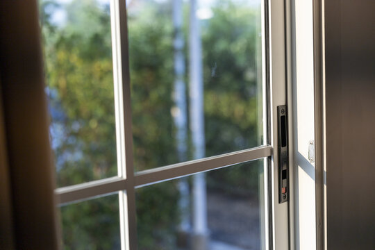 Peaceful bright sliding glass window partly open showing calm green nature tree outside with aluminum frame interior house room architecture design detail providing fresh air and sunlight