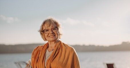 Fototapeta premium Senior woman smiling enjoying sunset by water