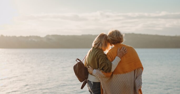 Senior women embracing enjoying sunset ocean view