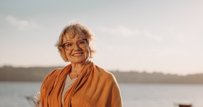 Senior woman smiling by lake at sunset