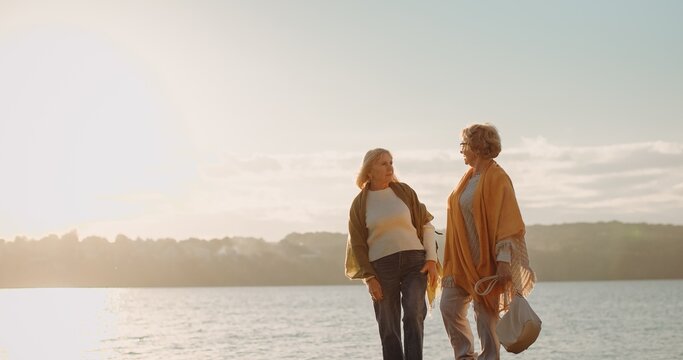 Two senior women friends walking by water at sunset
