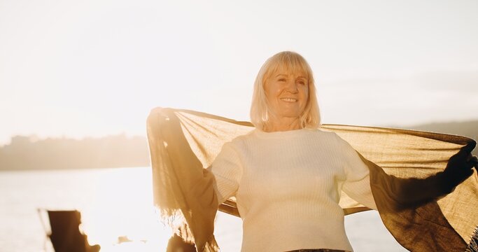 Senior woman enjoying freedom with blowing scarf at sunset