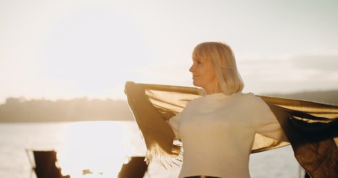 Senior woman enjoying freedom by the water during sunset