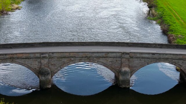Top view of multi arch stone bridge with symmetrical spans and reflections in river water. Empty roadway over river with classical construction and flowing current. Historic bridge pattern and