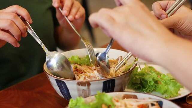People eating delicious asian noodle soup with spoon and fork, close-up.