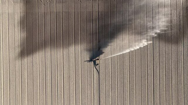 Irrigation pivot gun machine spraying water on an agricultural field during a dry and sunny spring day. Drone view from above.