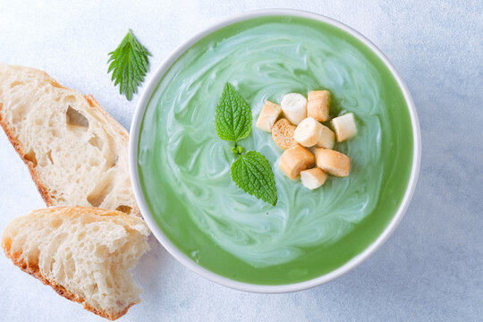 Close up of a bowl of mint or nettle leaves green soup sits on a blue background. The soup is swirled with cream, topped croutons, pieces of bread next to it. top view. top view. Healthy food