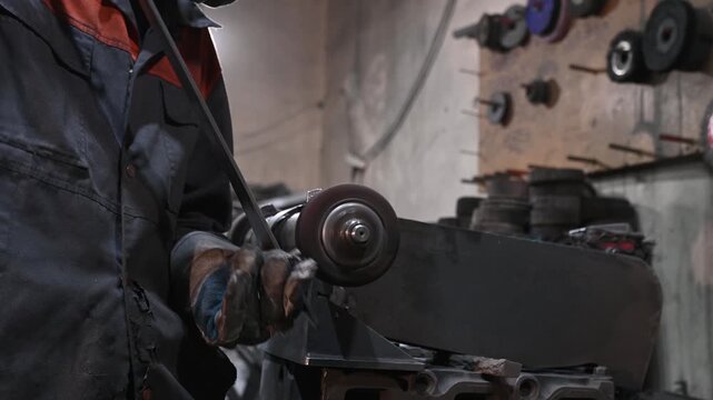 A stationary sharpening machine, grinding, sharpening, and metalworking in a garage workshop, manual work. The craftsman wears protective clothing, gloves, and goggles.