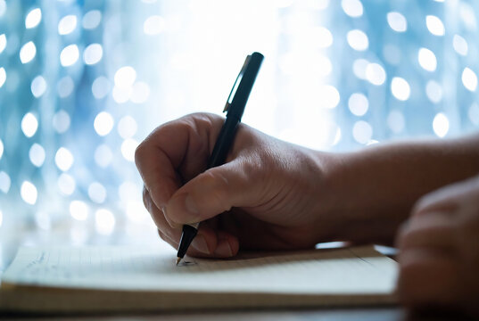 A hand is writing on a piece of paper with bokeh lights in the background.