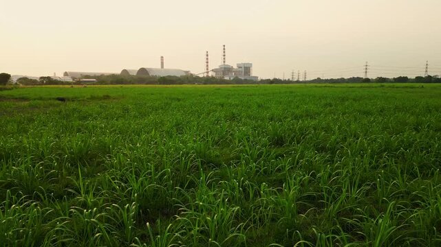 Push-in drone shot approaching the Calaca power plant under the greenfields with bright sky.
