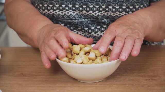 Adding crispy croutons into bowl for Caesar salad. Mixing toasted bread cubes for salad preparation. Preparing golden croutons as topping for Caesar dish. Handling crunchy bread pieces for salad