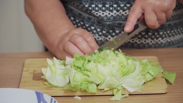 Chopping fresh lettuce leaves on wooden board for Caesar salad. Cutting crisp greens into smaller pieces for salad preparation. Slicing vibrant lettuce to create salad base. Preparing leafy greens for
