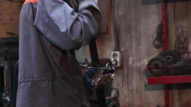A stationary sharpening machine, grinding, sharpening, and metalworking in a garage workshop, manual work. The craftsman wears protective clothing, gloves, and goggles.