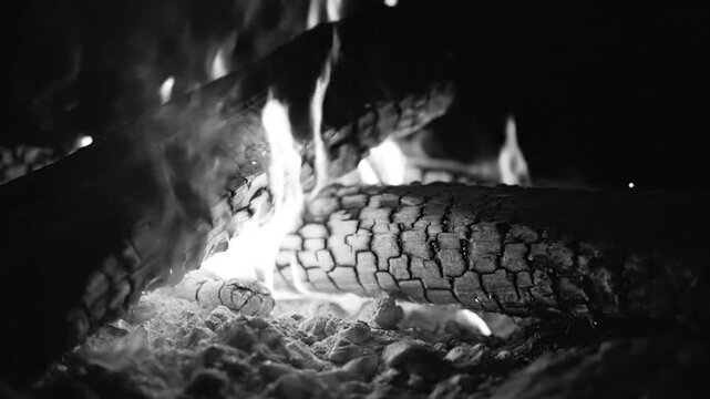 Black and white close up of burning wood logs with bright flames and glowing embers in a fireplace