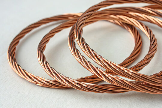 Close-up of twisted copper wire coils on white surface, metallic texture, warm brown hues