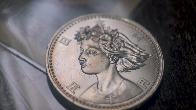 Cinematic close up video of a 1990 Japanese 5000 yen silver coin featuring an elegant female portrait with floral headdress and finely engraved relief.