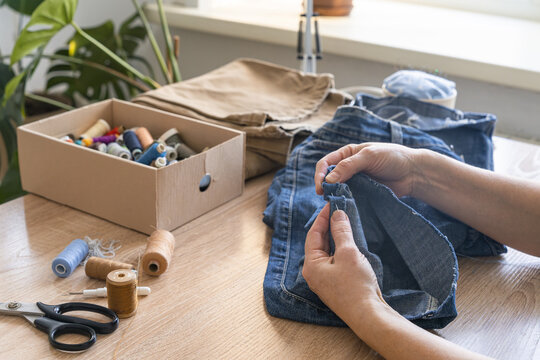Woman's hands sewing and repairing old denim jeans. Sustainable clothing repair, diy craft, and upcycling concept. Reusing things. Environmental awareness