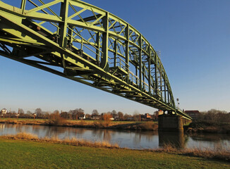 Naklejka premium Scenic view of a green iron truss bridge over the Weser river on a sunny day with clear blue sky in Nienburg, Germany