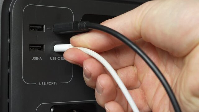 Close up of a man inserting USB C cable into portable power station. Device screen turns on showing charging and power supply in use.