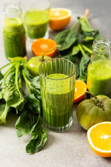Fototapeta premium Fresh juice is made using spinach, chard, and broccoli along with oranges and tangerines. A glass of green juice sits by fresh ingredients on a clean kitchen counter
