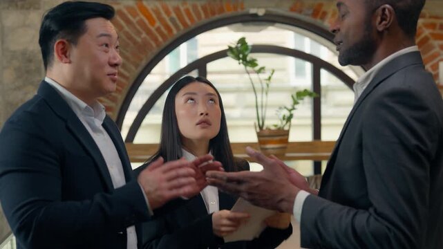 Three business multiracial businessmen team talking ignoring stressed businesswoman unequal rights discrimination African Asian colleagues in office communicate Japanese woman with papers irritated