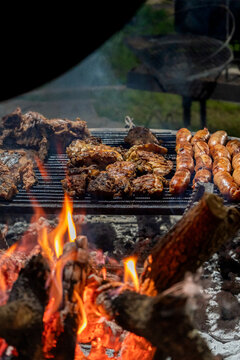 Vertical Shot of Meat and Sausages Grilling Over Large Wood Flames