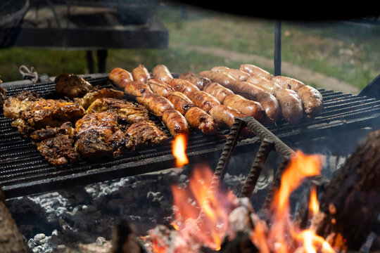 Meat and Rows of Sausages Grilling over Embers and Open Fire