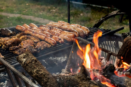 Rows of Sausages Grilling on a Charcoal Barbecue with Bright Flames