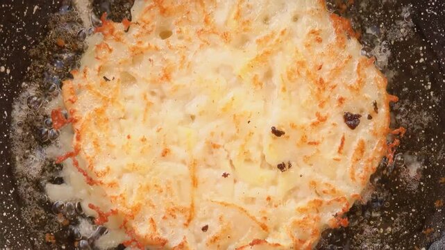 Wooden spatula flipping a raw potato pancake to the crispy golden brown side on a hot skillet. Delicious draniki.