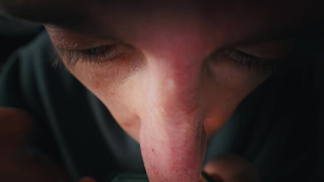 A young man intensely stares at a glowing computer screen in a dark room late at night. Concept of digital addiction, late night gaming, insomnia, and modern cyber security hacking.