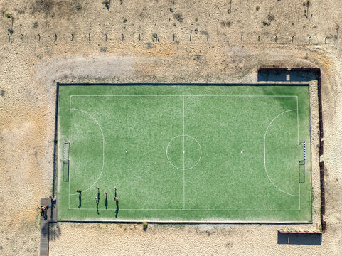 Aerial view of a vibrant green football field standing out against the pale, sandy surroundings, Praia do Molhe Norte, Figueira da Foz, Portugal.