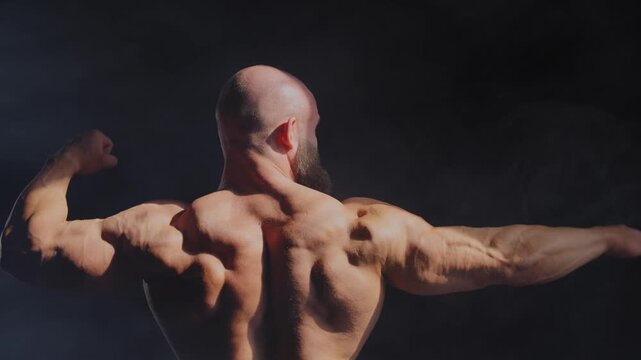 A male bodybuilder poses in shorts, showing off his back muscles.