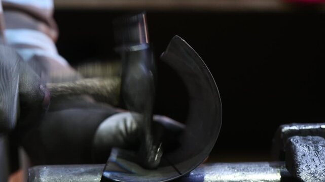 Cold forging of metal by hand, shaping the piece with a hammer on an anvil. Metalworking. Handcrafting historical fencing armor in a workshop. Traditional craft.